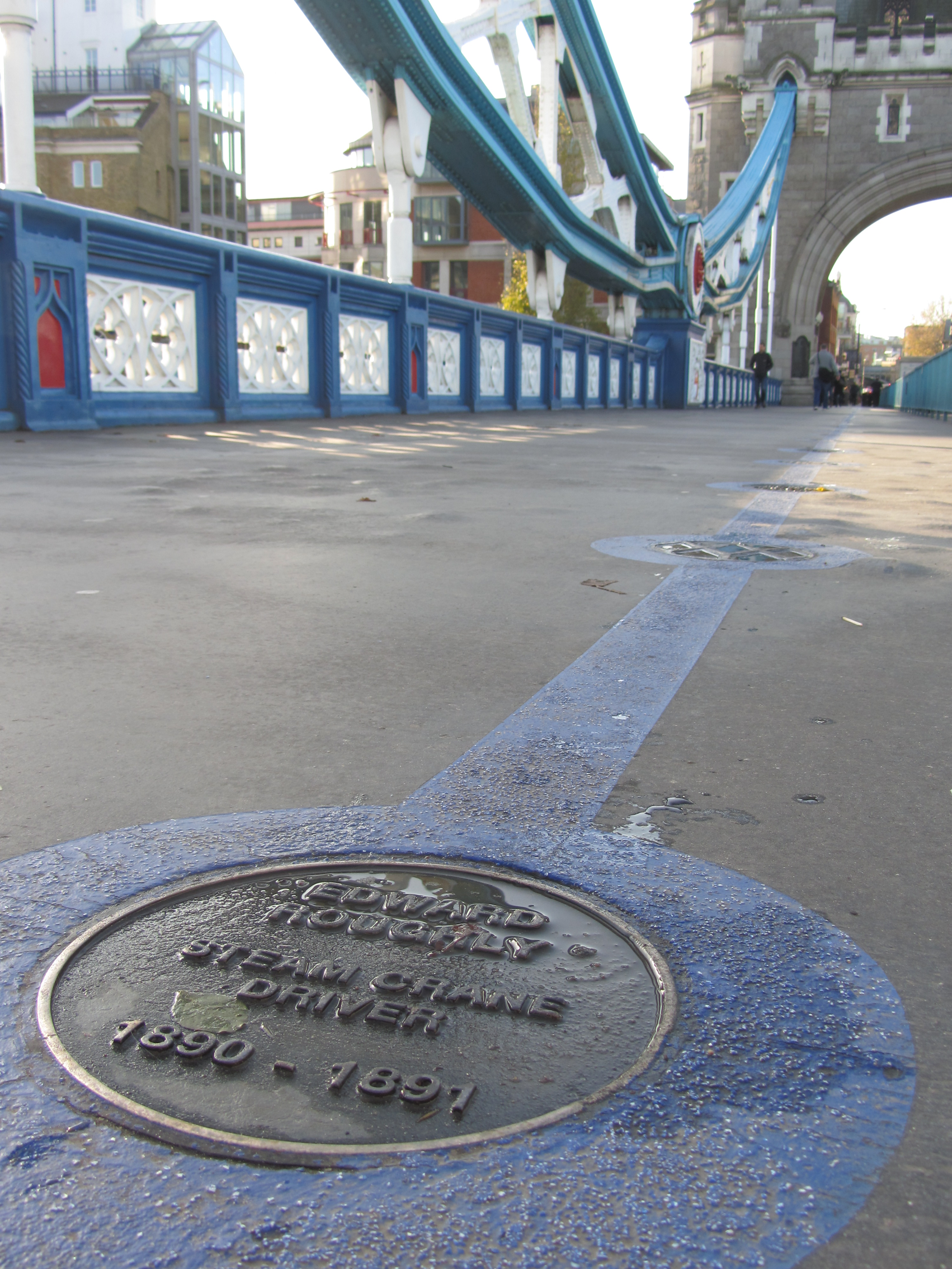 photograph of a brass plaque in a blue painted line leading across the walkway on Tower Bridge